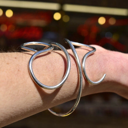 Vintage sterling silver wire wrap cuff bracelet on a person's wrist, featuring minimalist solid silver swirls. Adjustable bohemian jewelry, approximately 7 1/2 inches in length.