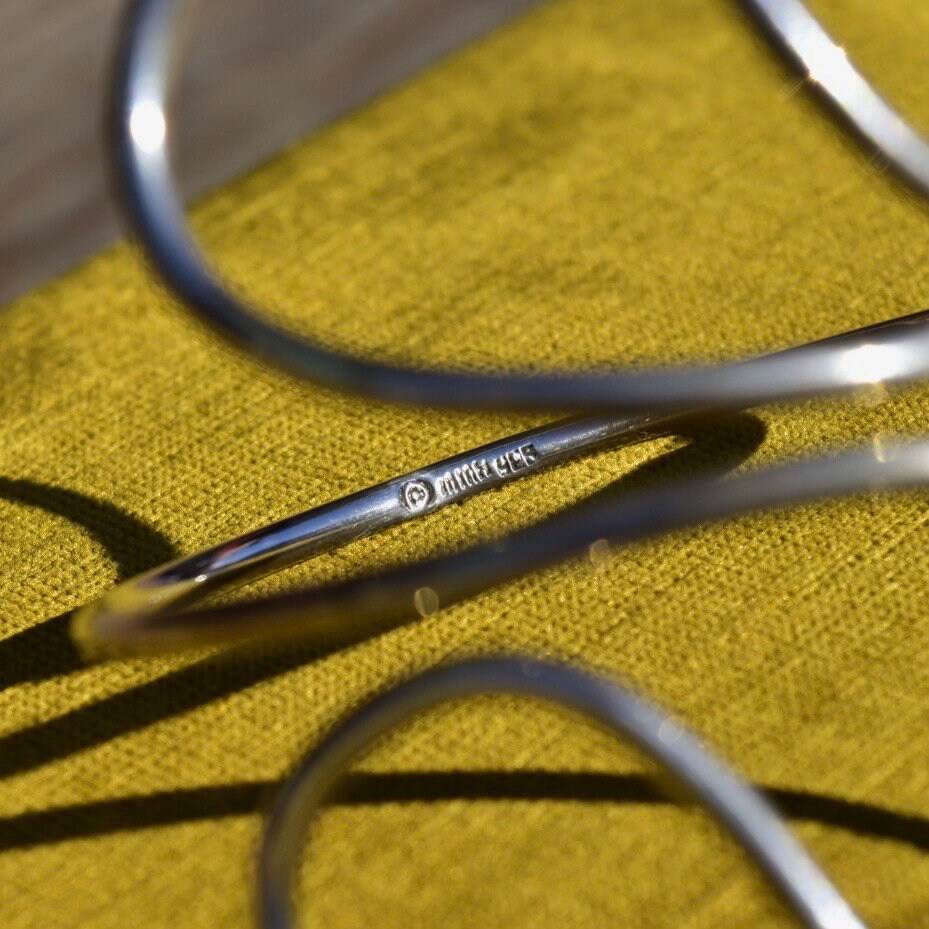 Vintage sterling silver wire wrap cuff bracelet on mustard yellow fabric background, minimalist boho style adjustable solid 925 silver swirl design, 7.5 inches long.