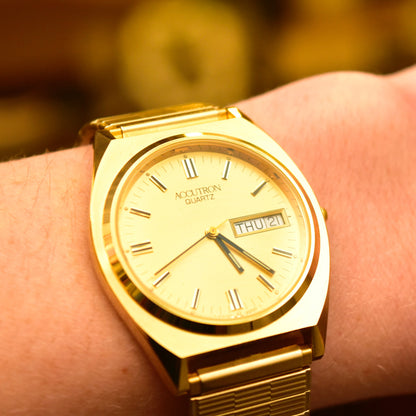 Vintage 1988 Bulova Accutron gold-tone Swiss quartz watch with day/date display, shown on a wrist with original box and papers, featuring a Speidel two-tone stretch band and measuring 7 inches.