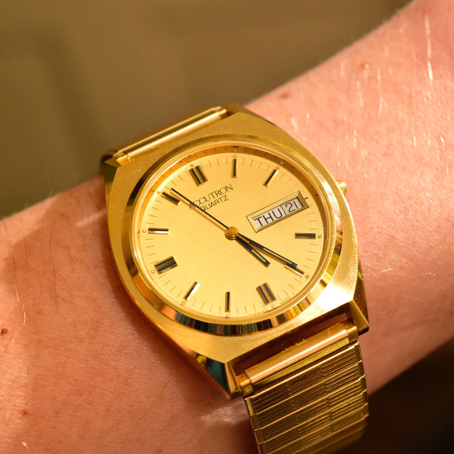 Alt text: Vintage 1988 Bulova Accutron gold-tone Swiss quartz wristwatch with day/date display, mounted on a wrist showing the watch face and Speidel two-tone stretch band.