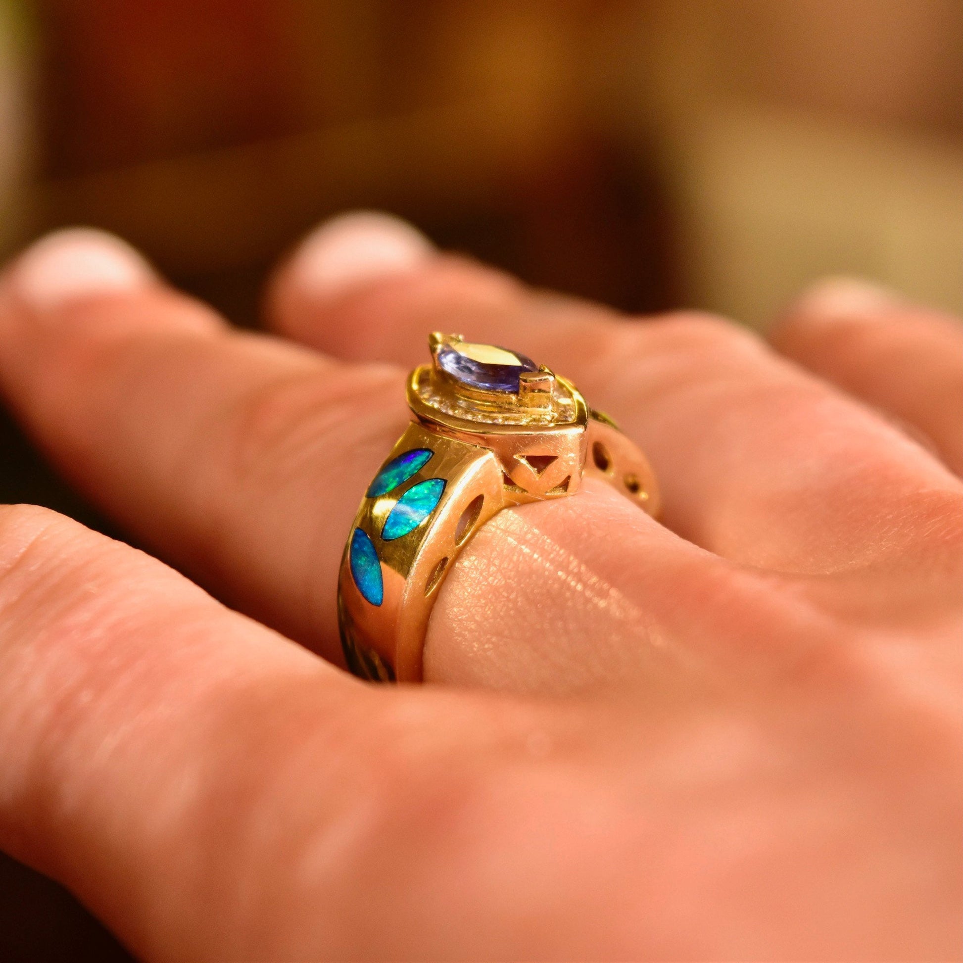 14K gold ring with marquise-cut tanzanite center stone surrounded by diamond halo and blue opal inlay on the band, worn on a finger