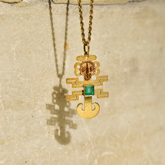 18K yellow gold Mayan Aztec sun god pendant necklace featuring an emerald-cut green gemstone, textured gold figure design, and delicate chain, 36mm in size.