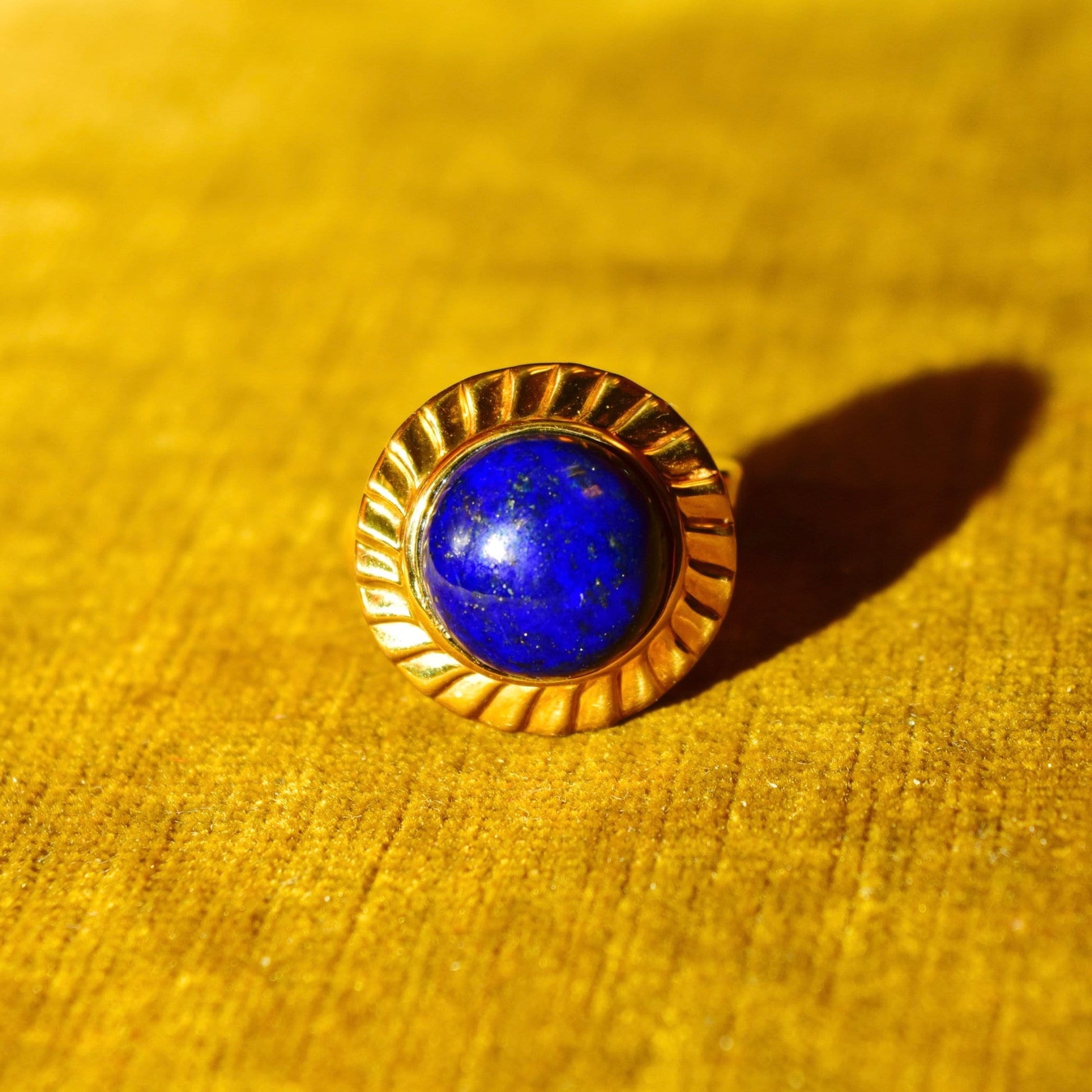 14K yellow gold cocktail ring featuring a vibrant cobalt blue lapis lazuli cabochon gemstone set in a fluted hollow band, sized 7 1/2 US, showcased on a textured golden fabric background
