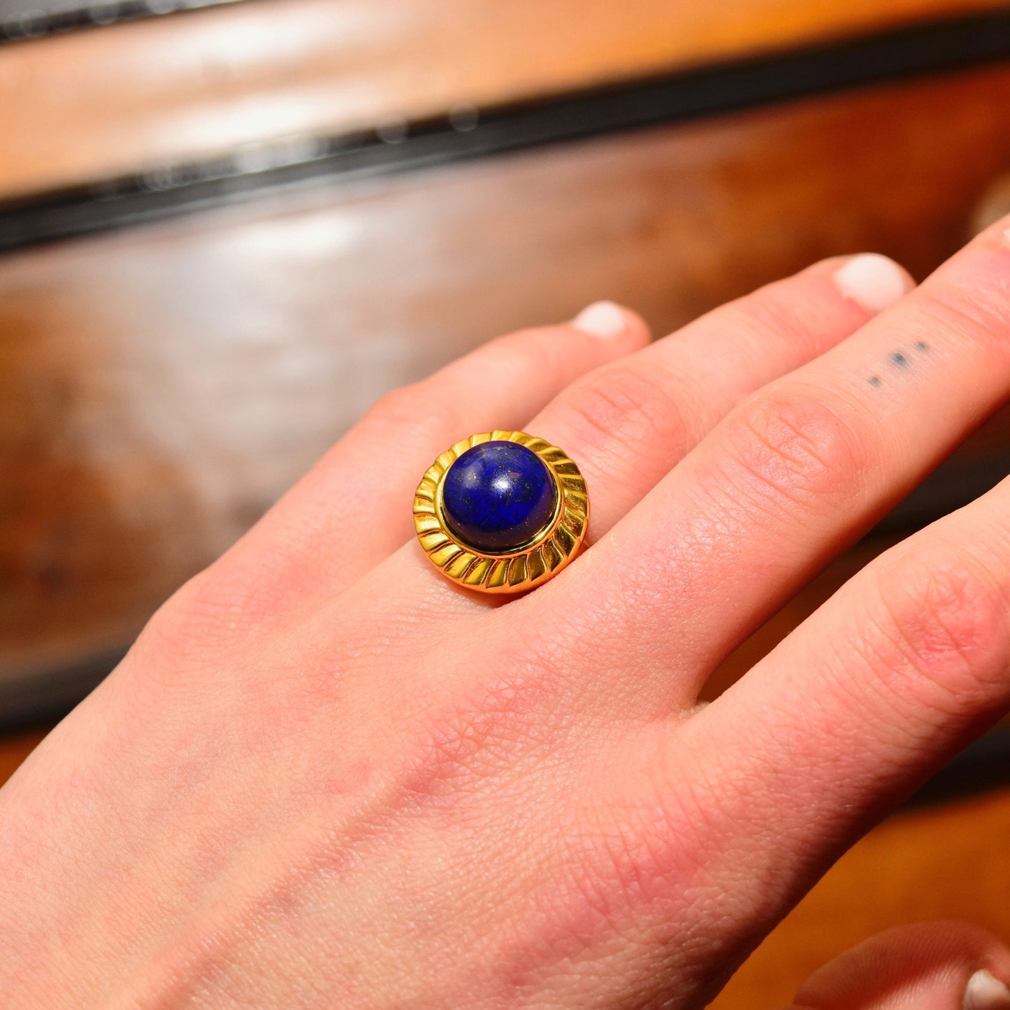 14K yellow gold cabochon lapis lazuli cocktail ring on a hand, with a round deep blue lapis lazuli gemstone set in a textured gold bezel setting, worn on the ring finger, size 7 1/2 US.