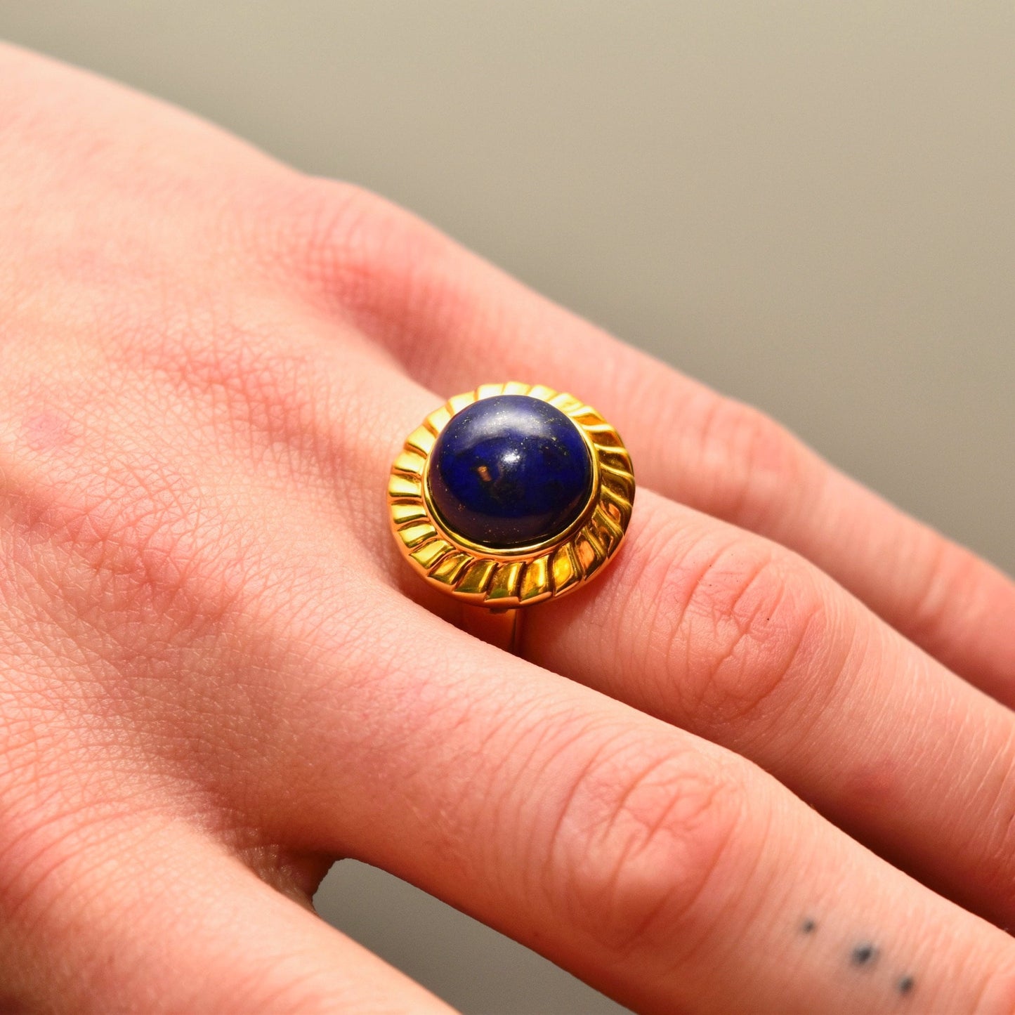 14K yellow gold cocktail ring with a round cobalt blue lapis lazuli cabochon gemstone solitaire, worn on a finger, size 7 1/2 US.