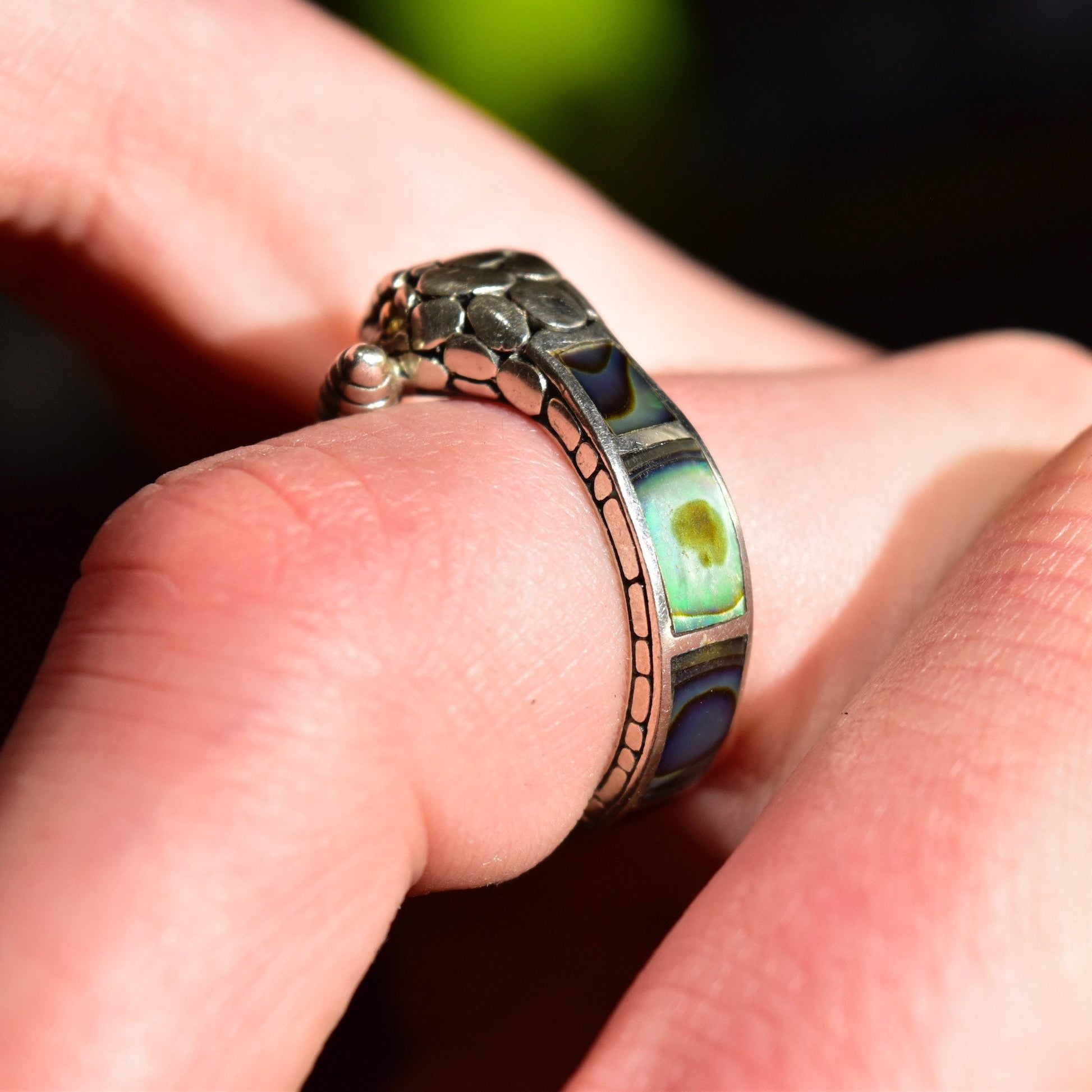 Vintage sterling silver snake ring with 18K gold accents and iridescent abalone shell inlay, depicting a coiled rattlesnake with engraved details and gold eyes, shown on a finger against a dark background.