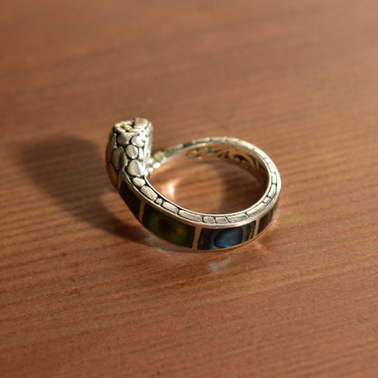 Vintage sterling silver snake ring with 18K gold-eyed rattlesnake coil design and abalone shell inlay, in a close-up view on a wooden surface.