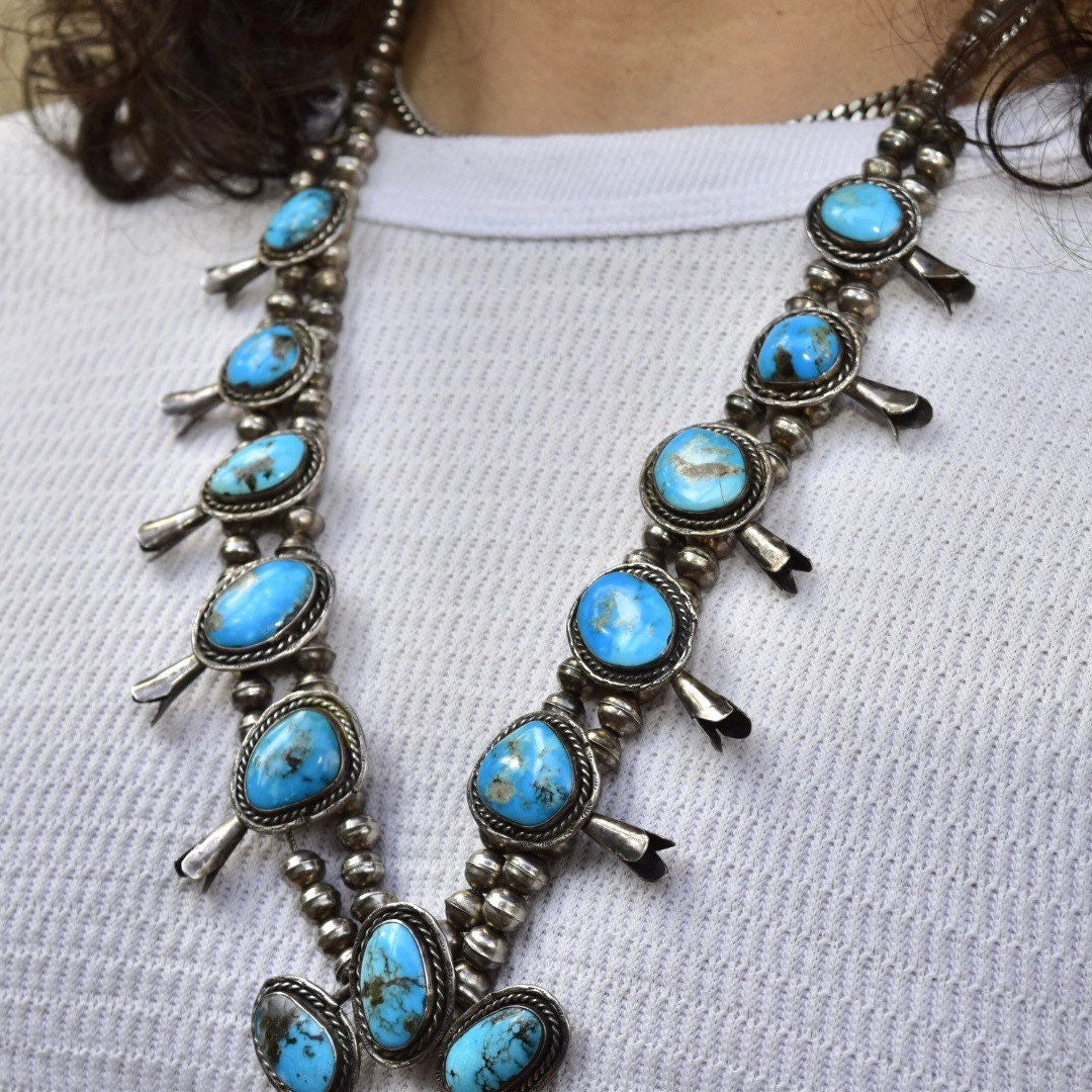 Vintage Navajo squash blossom necklace with natural blue turquoise stones set in coin silver, Old Pawn Native American jewelry, measuring 29 inches in length, displayed on a textured fabric background.