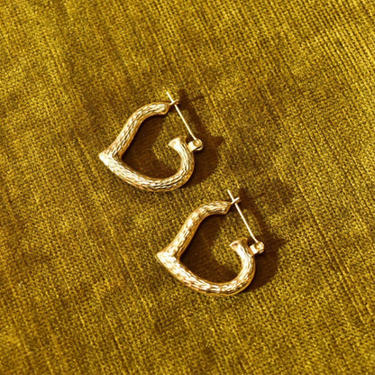 14K yellow gold textured heart hoop earrings on gold fabric background