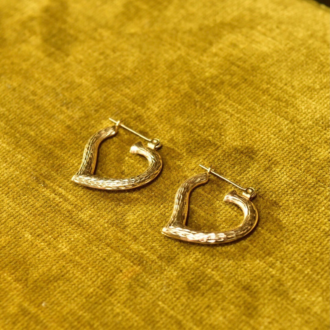 Vintage 14K yellow gold hammered heart hoop earrings on textured gold fabric