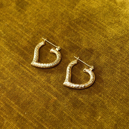 Vintage 14K yellow gold hammered textured heart hoop earrings, 22mm in size, laying on golden fabric background.