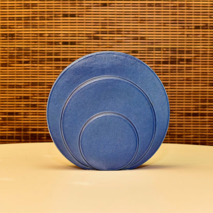 Vintage Art Deco Trenton Potteries rare blue ceramic 'Circlet' modernist circle disk sculpture vase designed by G. McStay Jackson, measuring 8 1/2 inches tall, against a woven wicker background.