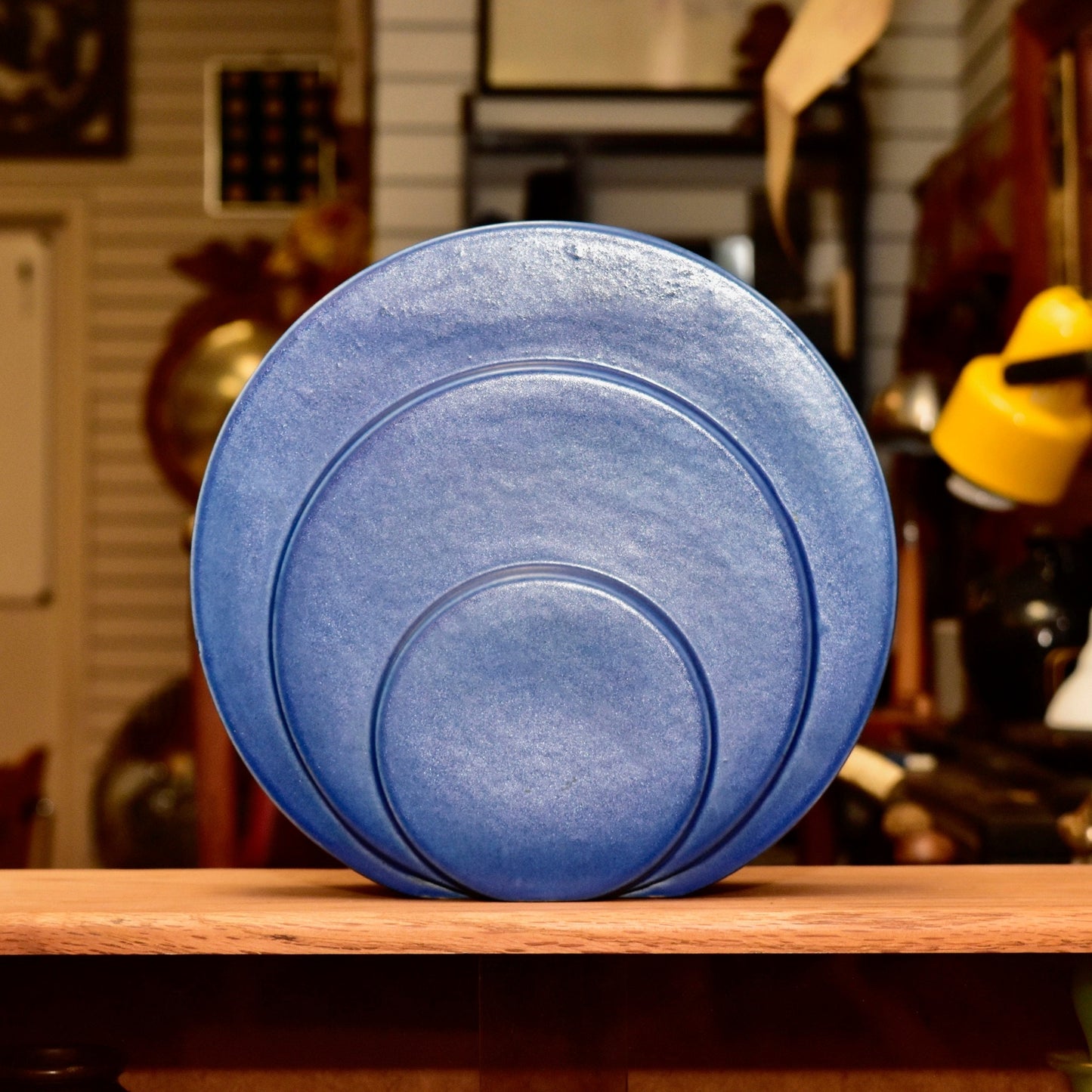 Vintage Art Deco blue ceramic Circlet vase designed by G. McStay Jackson for Trenton Potteries, featuring modernist circular disk sculpture, 8 1/2 inches tall, displayed on a wooden shelf with blurred home decor in the background.