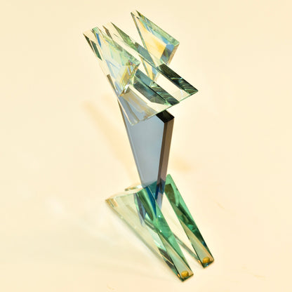 Abstract modernist glass sculpture with angled geometric shards in shades of blue, green and gold arranged in a dynamic composition on a clear glass base, created by American studio glass artist Stephen Jon Clements in 1989.