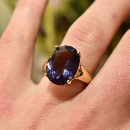 Vintage gold-plated sterling silver ring with a large oval-cut blue gemstone worn on a finger, 925 gold-tone cocktail ring, size 7 US.