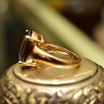 Vintage gold-plated sterling silver ring with an oval-cut simulated blue gemstone, showing intricate detailing on the band. The picture focuses on the ring from a close-up angle with a blurred background, emphasizing the metal's luster and gemstone's color.