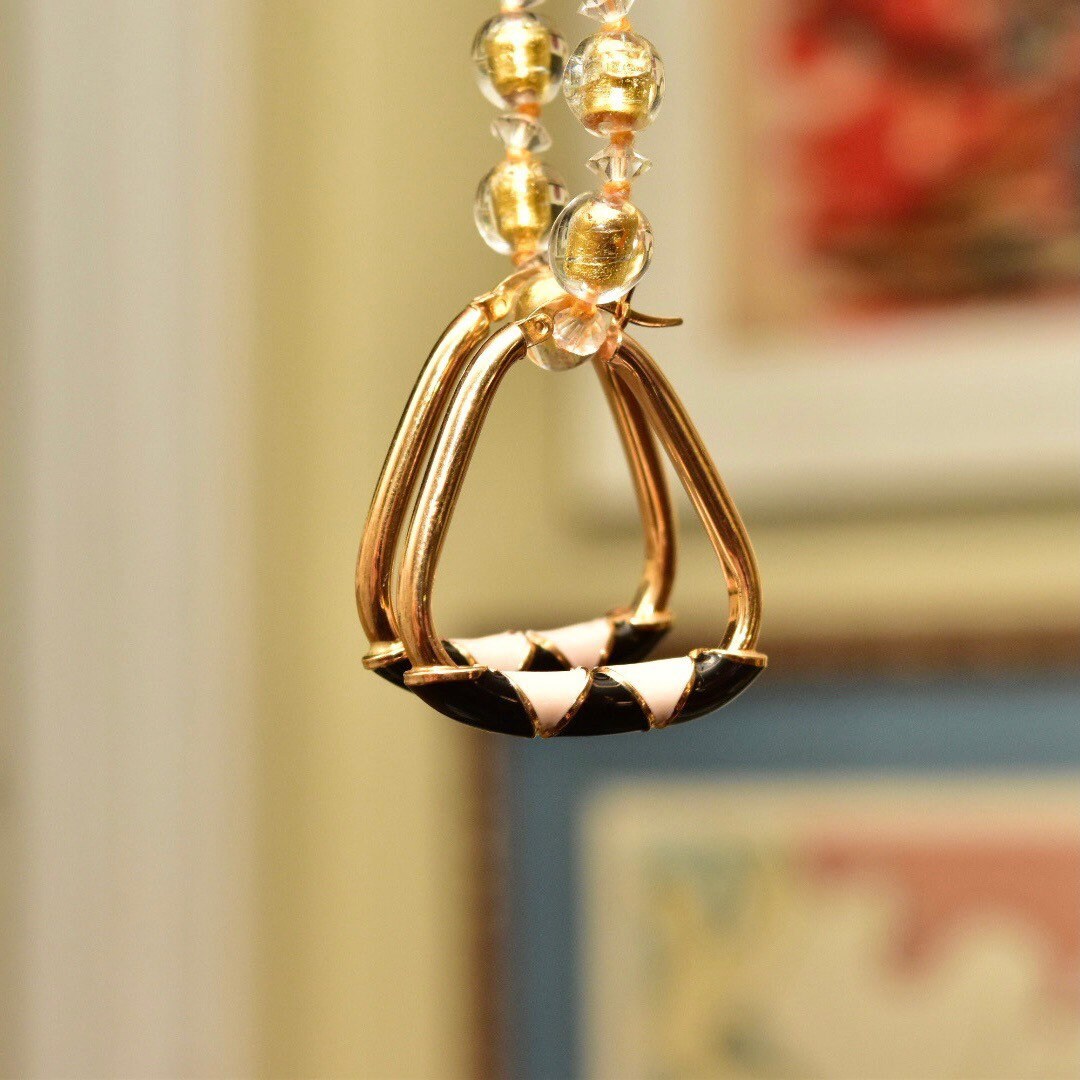 14K gold modernist triangle hoop earrings with black and beige enamel designs hanging in front of framed artwork