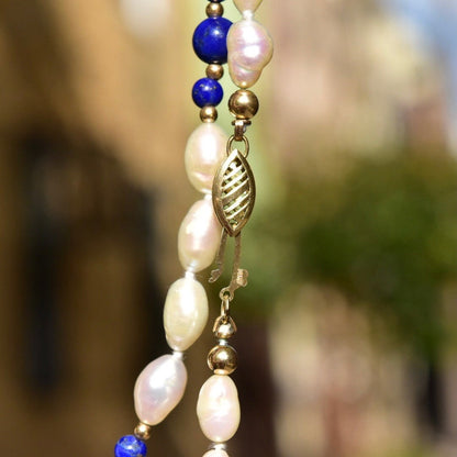 Vintage 14K fresh water pearl and lapis lazuli beaded necklace with baroque pearls, polished lapis lazuli beads, and gold accents hanging against a blurred background.