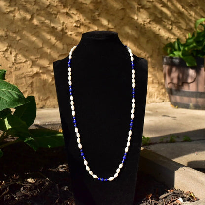 Vintage 14K gold necklace with knotted fresh water baroque pearls and polished lapis lazuli beads, accented by gold beads, measuring 29 inches long, displayed outdoors on a black jewelry stand.