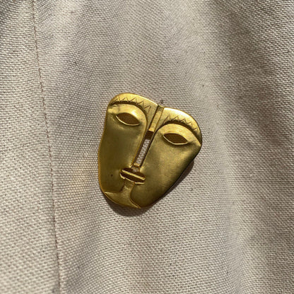 Vintage gold-toned abstract face mask brooch pin with engraved tribal design, unique modernist style jacket accessory, measures 45 mm.