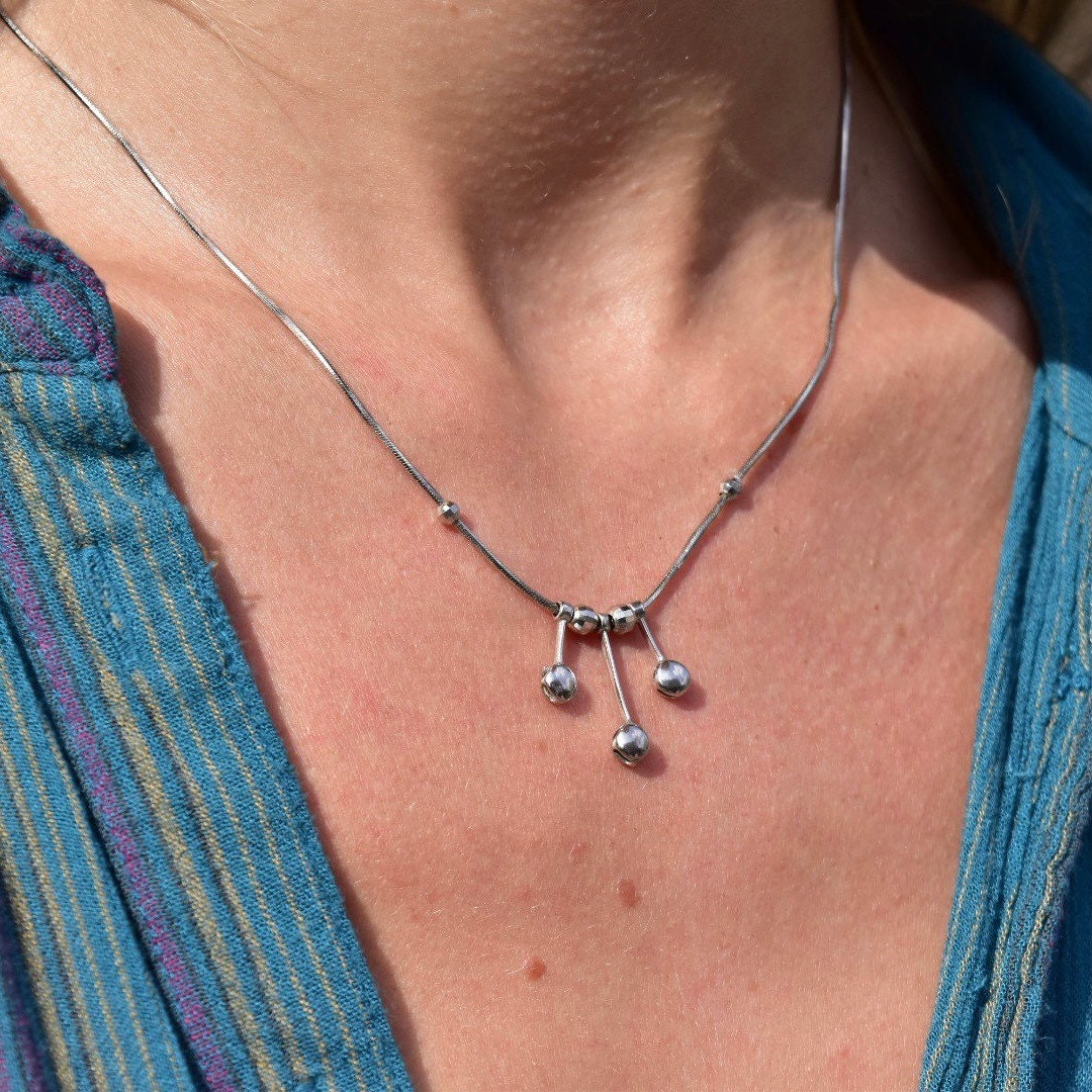 Vintage Italian 14K white gold tassel necklace with multi-bead tassel pendant on a thin gold snake chain, worn on a woman's neck against a blue sweater.