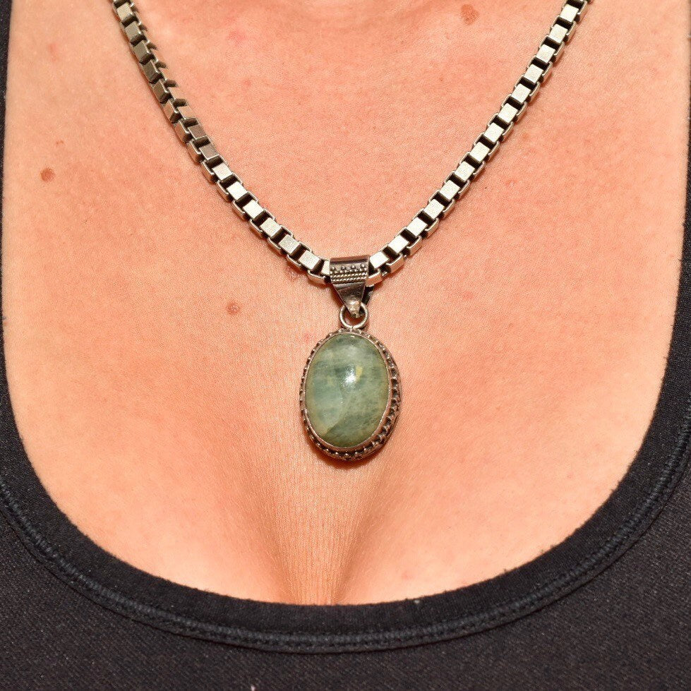 Vintage Bohemian sterling silver necklace with green quartz pendant featuring ornate Balinese design, worn on a person's chest against black shirt.