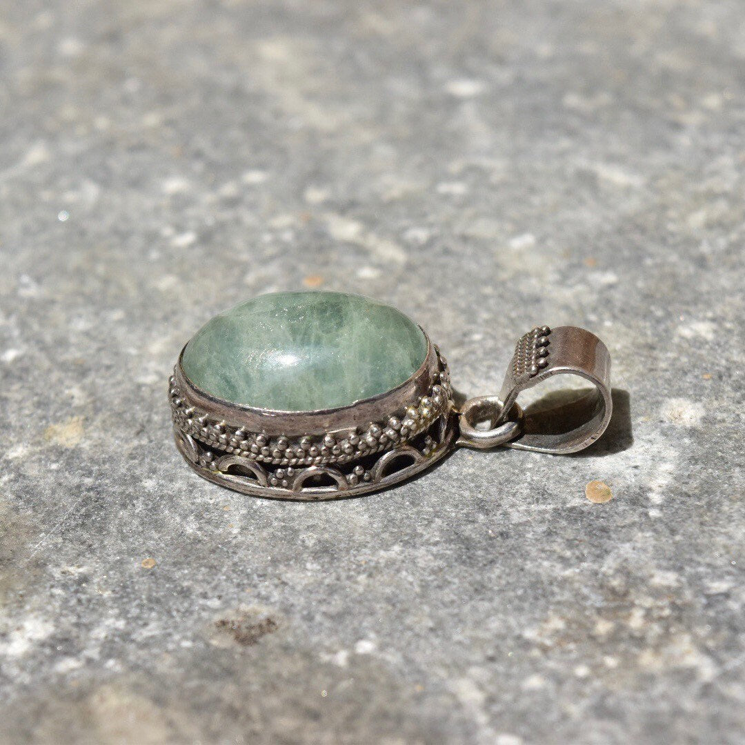 Vintage Bohemian sterling silver pendant with green quartz cabochon and intricate Balinese design, measuring 42mm in size, shown on textured gray background.