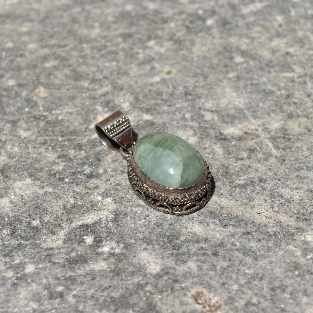 Vintage Bohemian sterling silver quartz pendant with Balinese design and green oval cabochon, measuring 42mm, on textured stone surface.