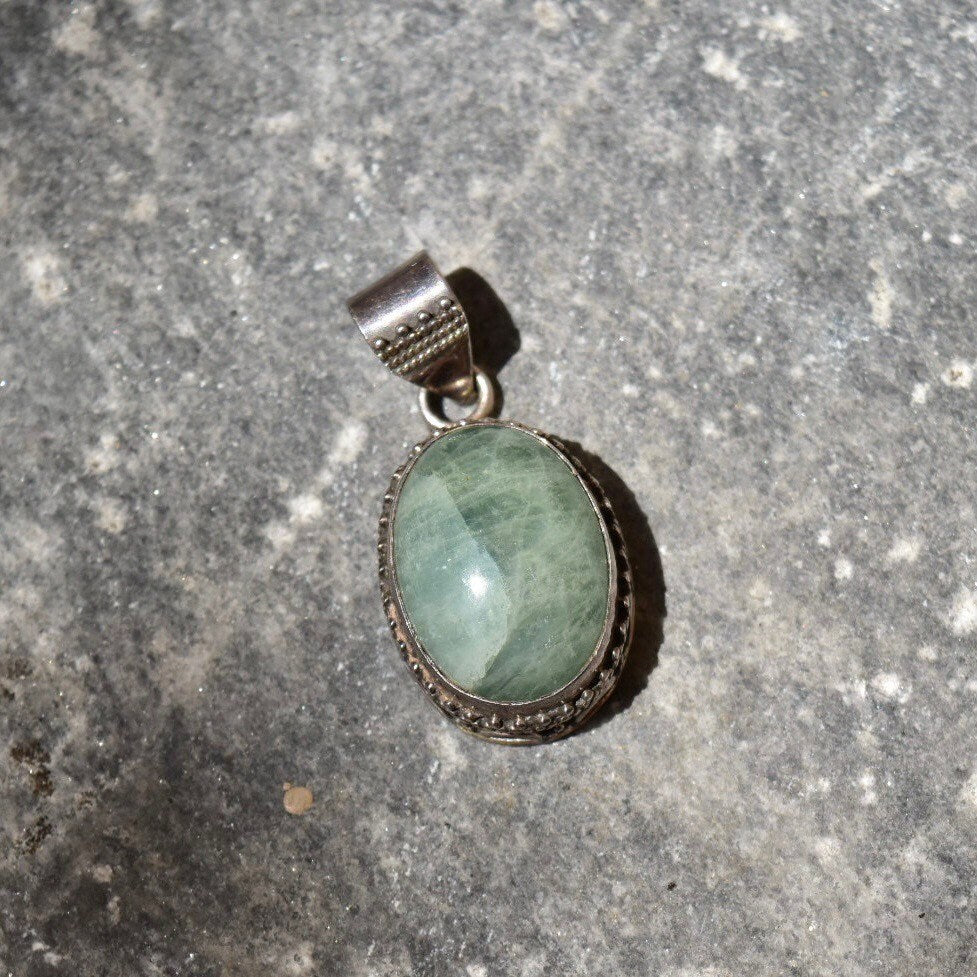 Vintage sterling silver pendant with green quartz cabochon in ornate Balinese design setting on textured gray background