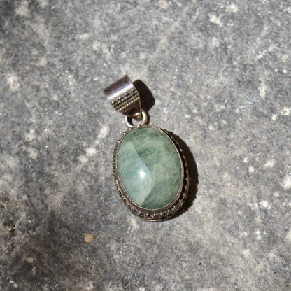 Vintage sterling silver pendant with green quartz cabochon in ornate Balinese design setting on textured gray background