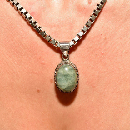 Silver chain necklace with oval green quartz cabochon pendant in ornate setting against peach skin background