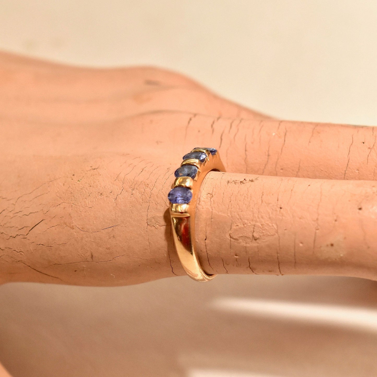 Vintage 14K yellow gold band ring featuring 4 round tanzanite stones set in a half-eternity style on a person's finger.