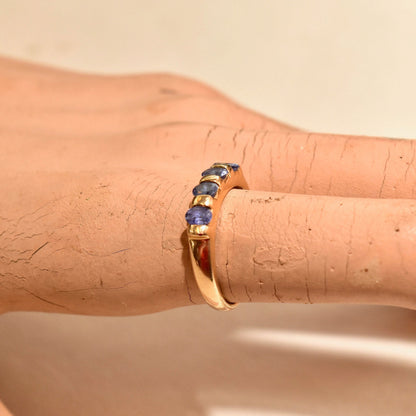 Vintage 14K yellow gold band ring featuring 4 round tanzanite stones set in a half-eternity style on a person's finger.