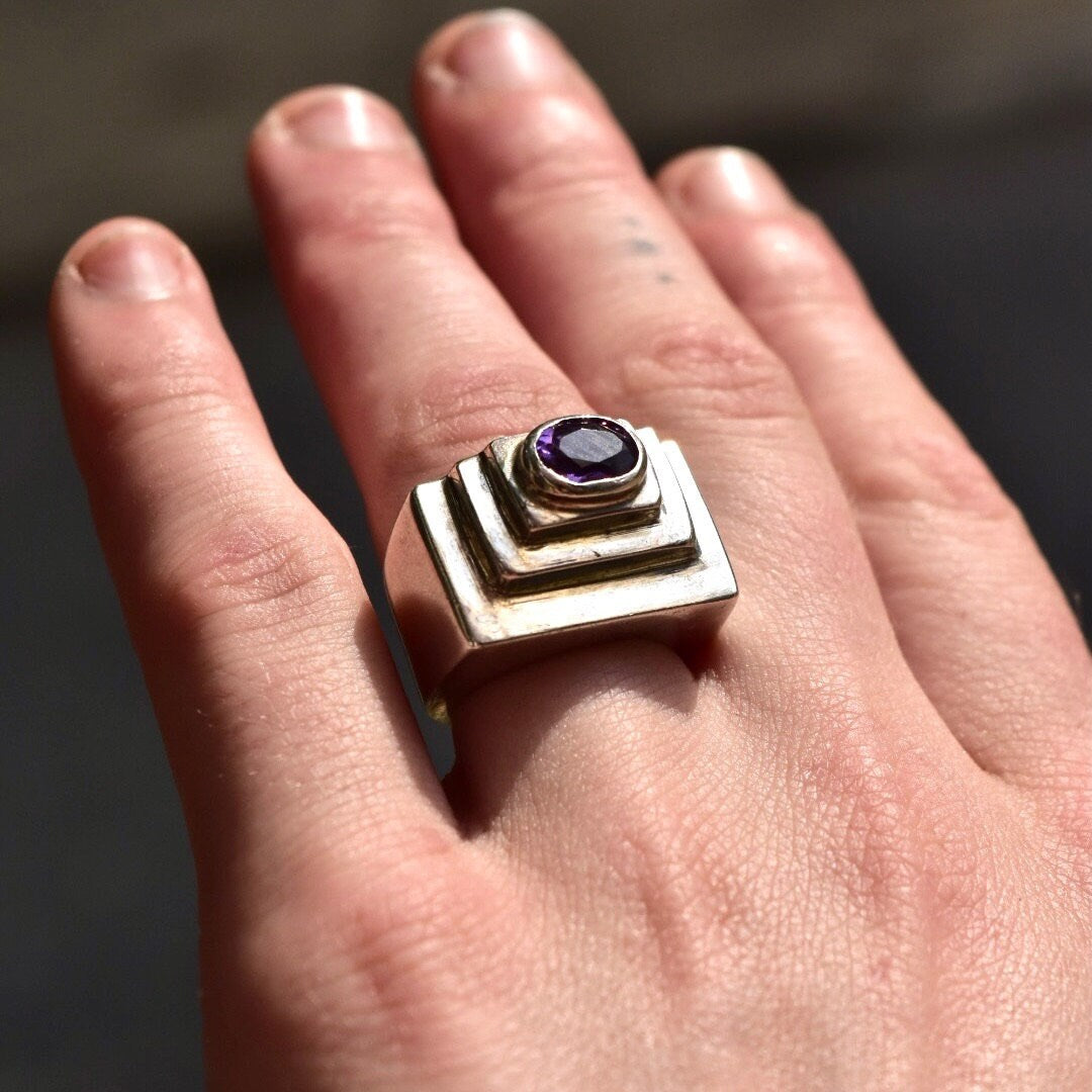 Vintage modernist sterling silver ring with an oval-cut amethyst gemstone set in a chunky, textured dome design featuring stepped detailing, shown on a hand, size 6 1/2 US.