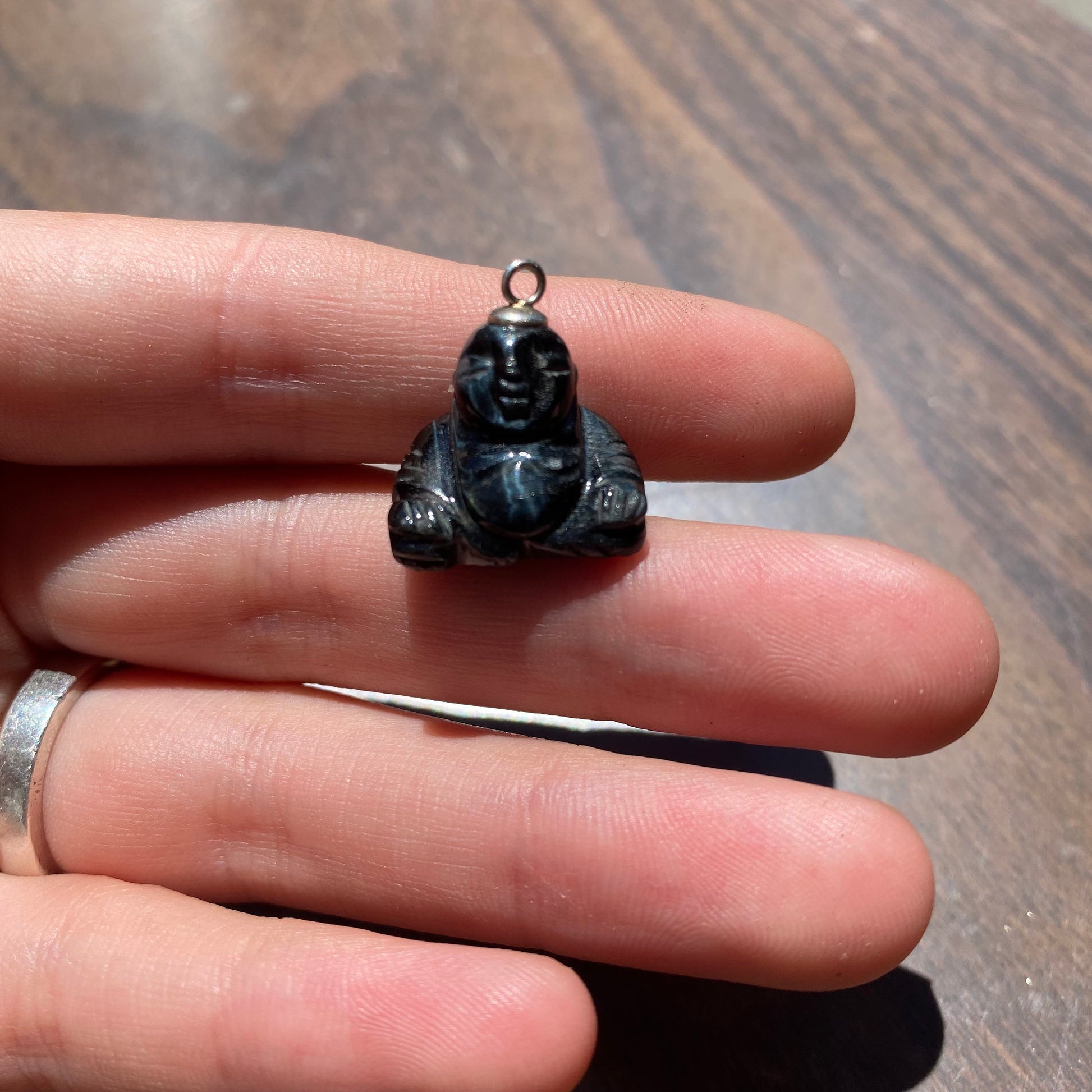 Vintage carved black stone Buddha charm pendant with silver loop held in palm of hand