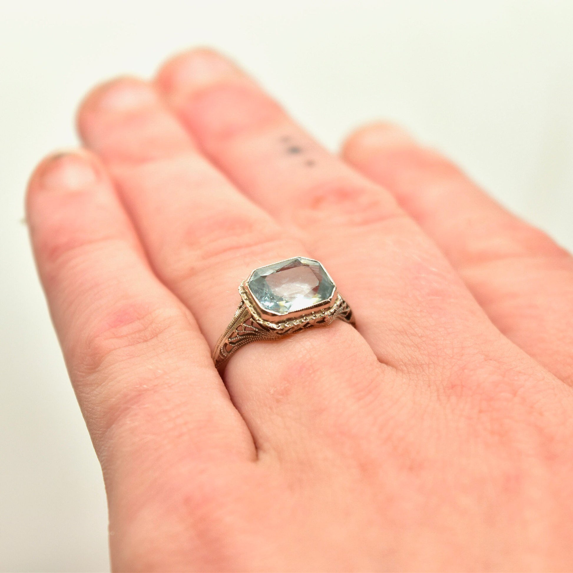 Antique Art Deco 14K white gold filigree ring with a faceted pale blue aquamarine gemstone in an intricate setting, worn on a hand. March birthstone ring, size 6 1/2 US.