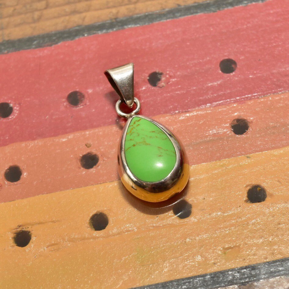 Vintage Mexican sterling silver teardrop pendant with lime green gaspeite gemstone set in polished silver drop setting on wooden surface