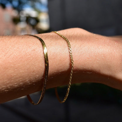 14K gold flat Bismark chain bracelets with different thicknesses on a person's wrist, showing the spring-ring clasp closure and minimalist jewelry style against skin.