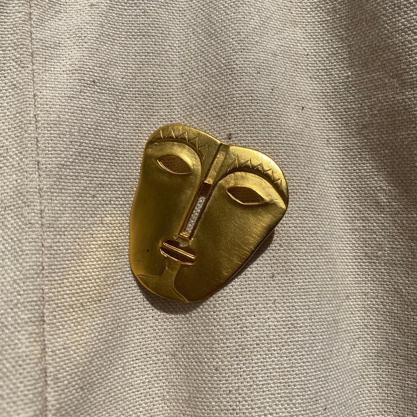 Vintage gold-toned abstract tribal face mask brooch pin with engraved modernist design, unique jacket accessory measuring 45 mm.