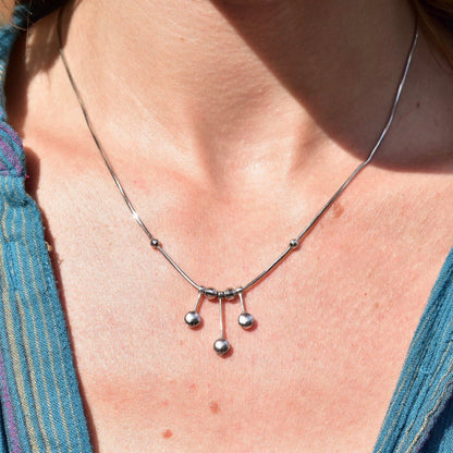 Close-up view of a woman wearing a vintage modernist Italian 14K white gold tassel necklace with a multi-bead tassel pendant hanging from a thin, delicate 1mm gold snake chain against her skin.