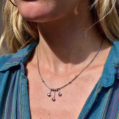 Vintage Italian 14K white gold tassel necklace with multi-bead tassel pendant on a thin gold chain, worn by a woman in a teal shirt, close-up view of the necklace and the woman's neck and lower face.