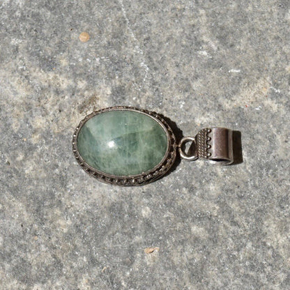 Vintage Bohemian sterling silver pendant with green quartz cabochon in ornate Balinese design setting on gray stone background