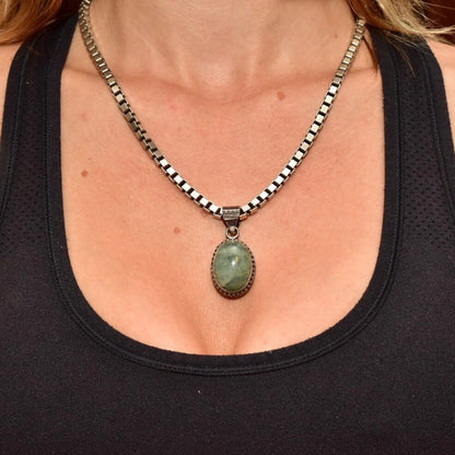 Vintage sterling silver pendant necklace featuring an oval green quartz cabochon set in an ornate Balinese-style bezel, worn on the neck of a woman in a black top.