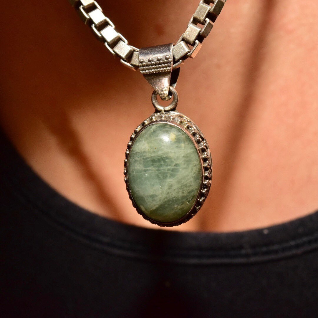 Vintage sterling silver pendant necklace with oval green quartz cabochon and intricate Balinese design, worn against black shirt