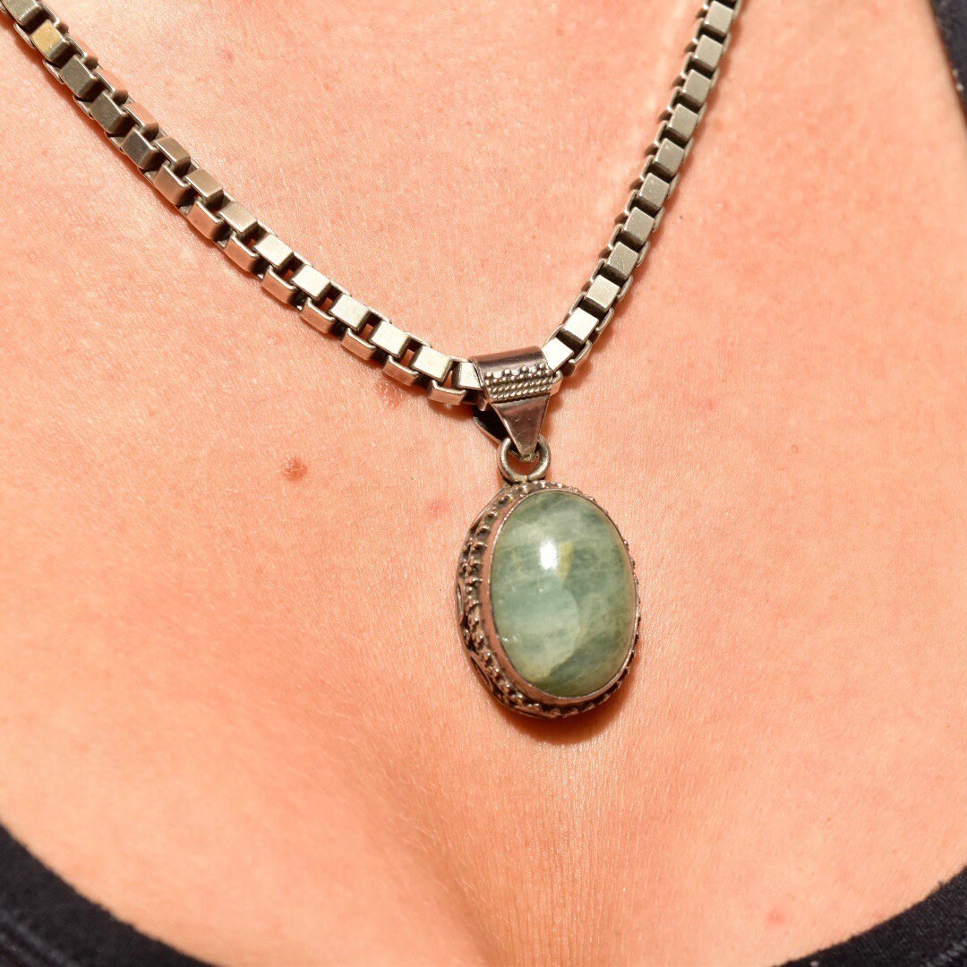 Vintage bohemian sterling silver necklace with oval green quartz pendant in ornate Balinese design, shown on person's chest against black shirt.