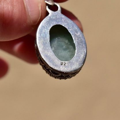 Vintage Bohemian sterling silver oval pendant with oxidized floral design holding a translucent green quartz cabochon, shown in a hand for scale