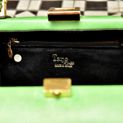 Vintage black leather barrel box purse with gold-toned hardware, green felt lining, and brass logo on a checkered floor