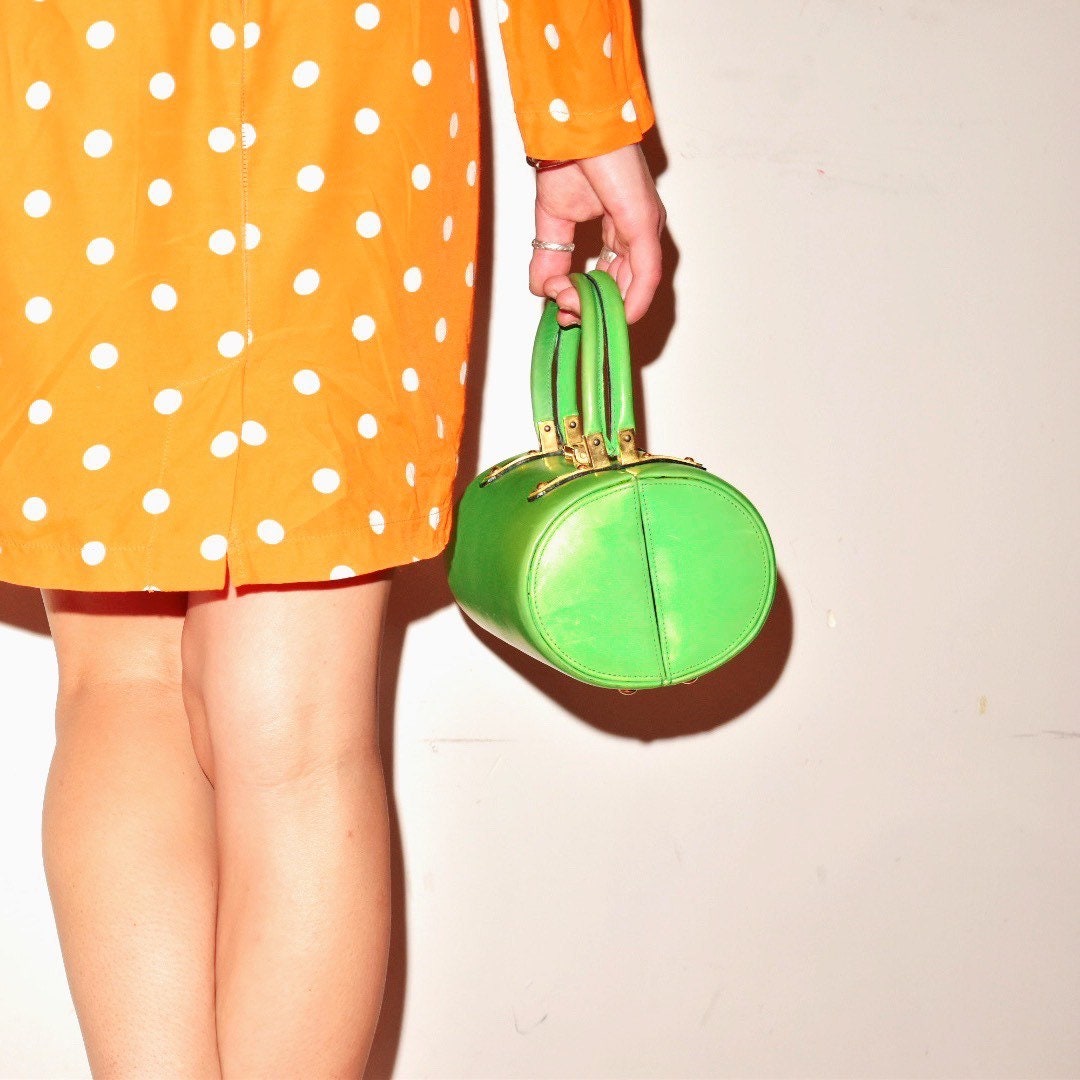 Vintage polka dot dress and green round leather handbag held by a woman's hand, showing fashion accessories from a retro or mid-century inspired style.