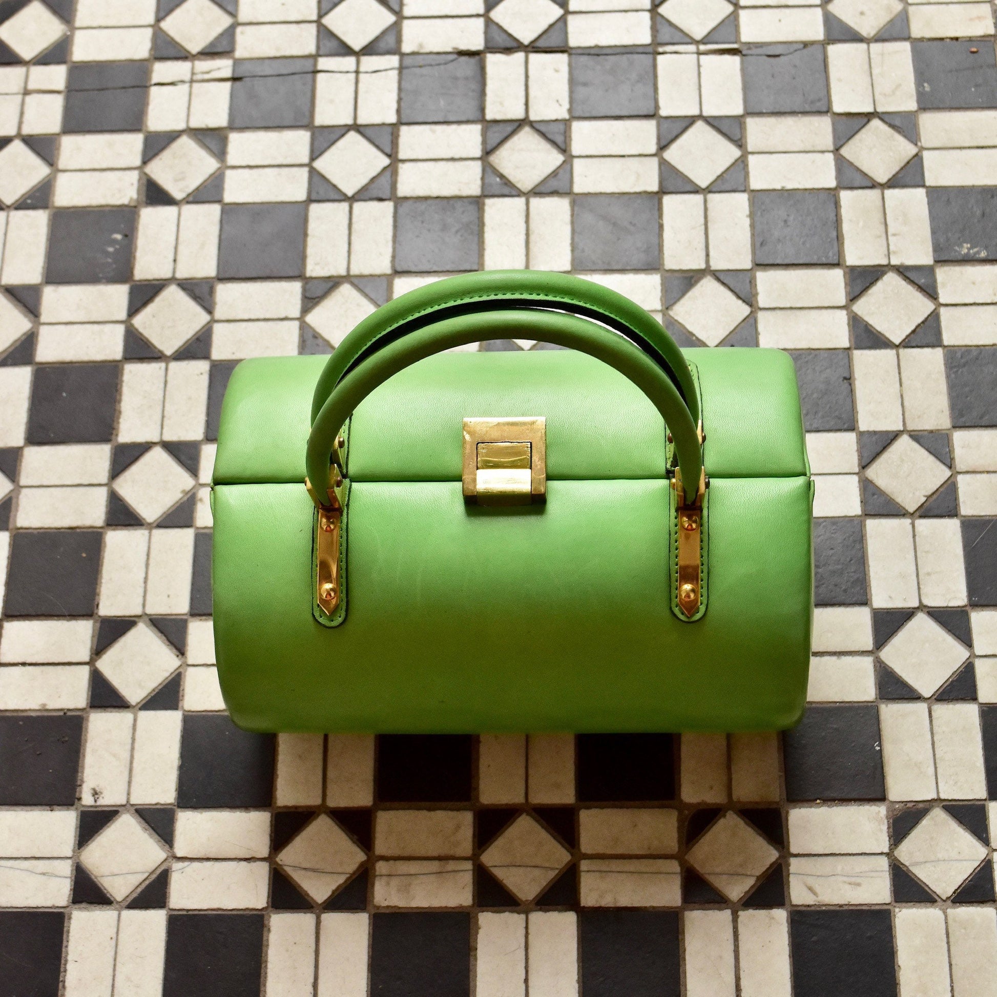 Mod TANO of Madrid lime green leather barrel box purse with brass hardware, retro hard shell top handle box bag, 8 1/2" wide, sitting on black and white geometric tiled floor