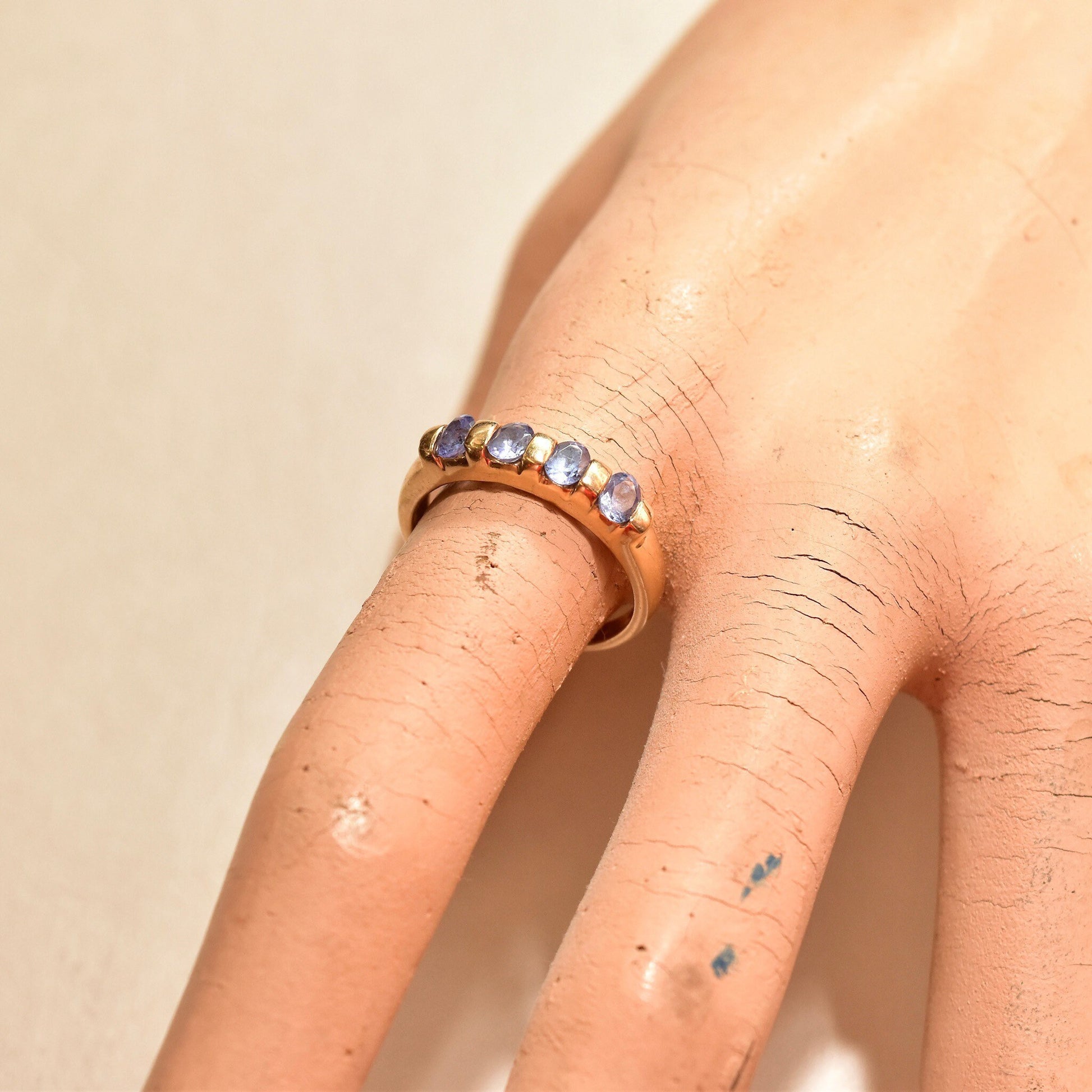 Vintage 14K yellow gold tanzanite band ring with 4 round tanzanite stones set in a half eternity style on a woman's finger, showing light patches of dry skin and ink markings